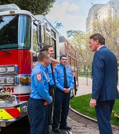 تین فائر مین اور گورنر فائر ٹرک کے سامنے کھڑے ہیں۔